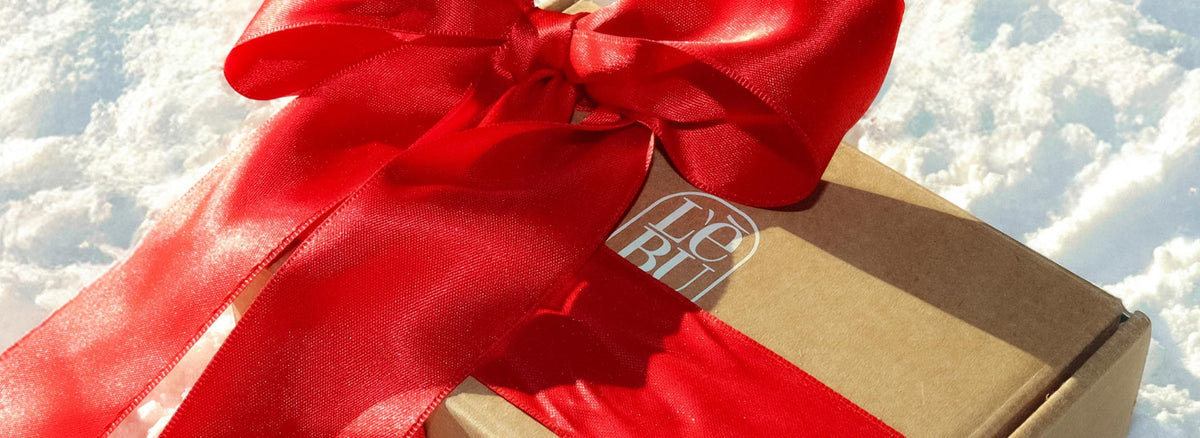 A styled flat-lay of winter snow with a Lebubè gift box and a ribbo, with inside Lebubè's hybrid skincare-infused makeup as a Christmas present