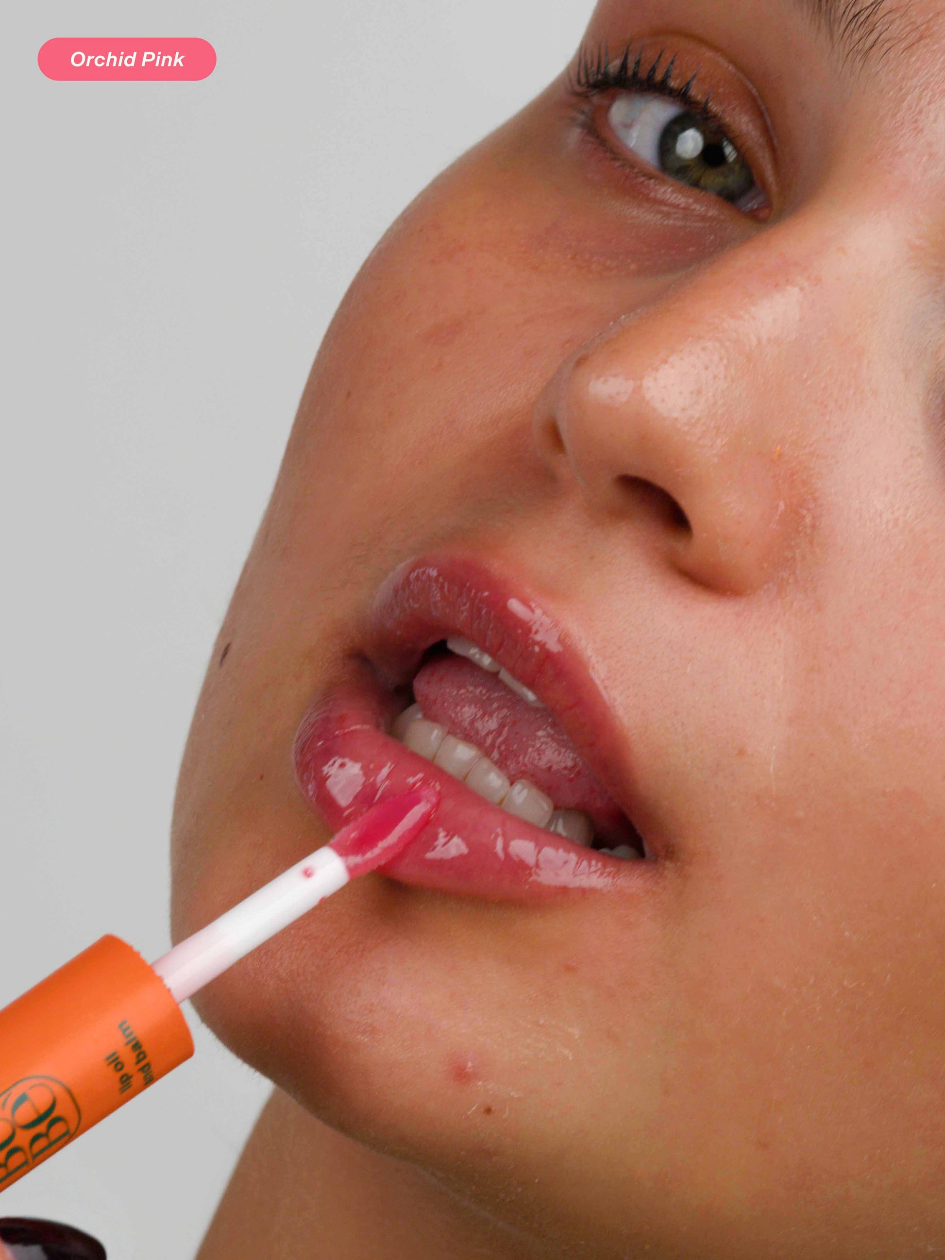 Woman applying the Halal, natural, glossy and hydrating lip balm in Orchid Pink, hydrating peptide lip treatment for dry lips