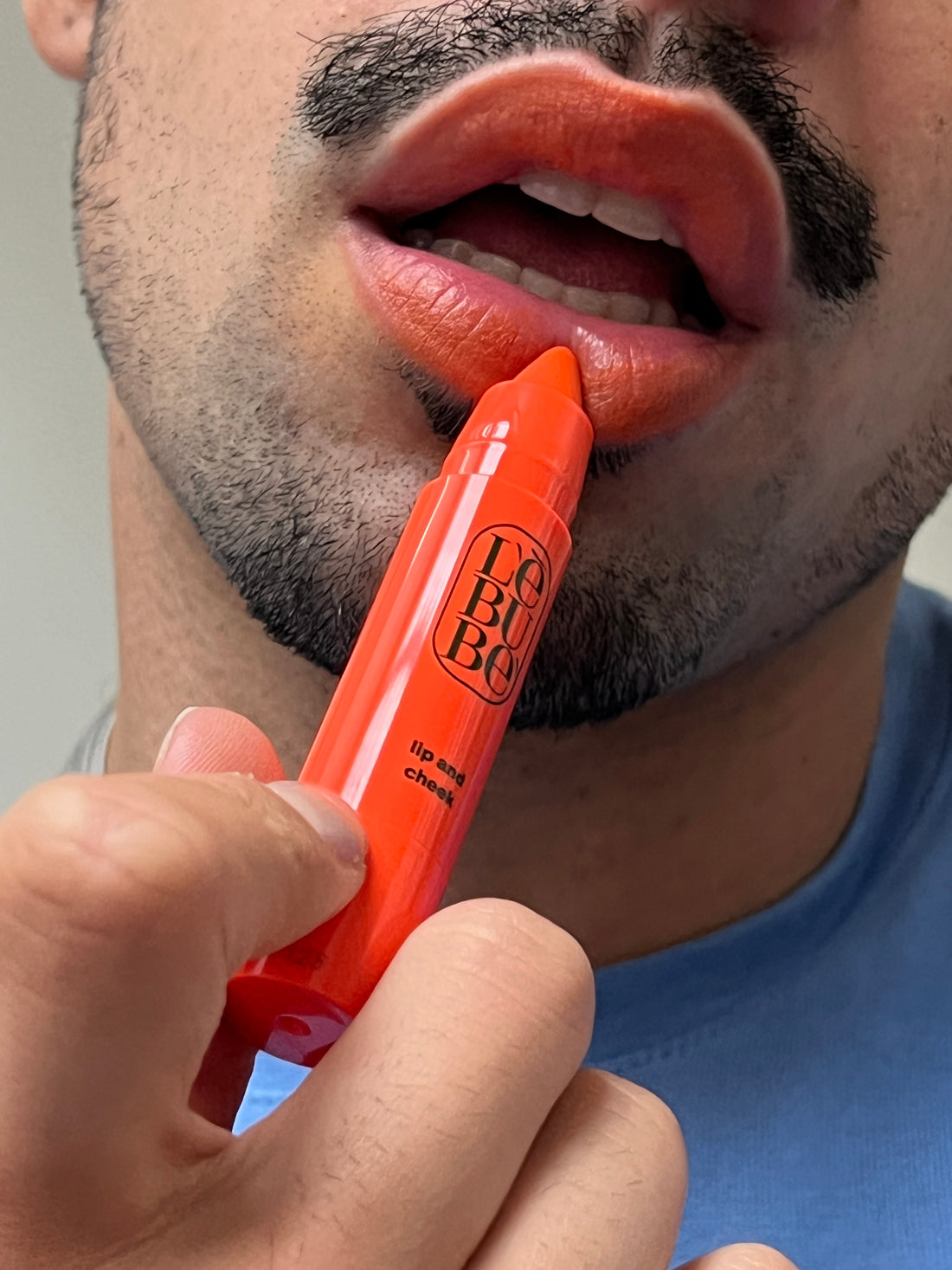 Man applying Lebubè vegan and natural hydrating orange lipstick on his lips for a sun-kissed after-the-sun effect