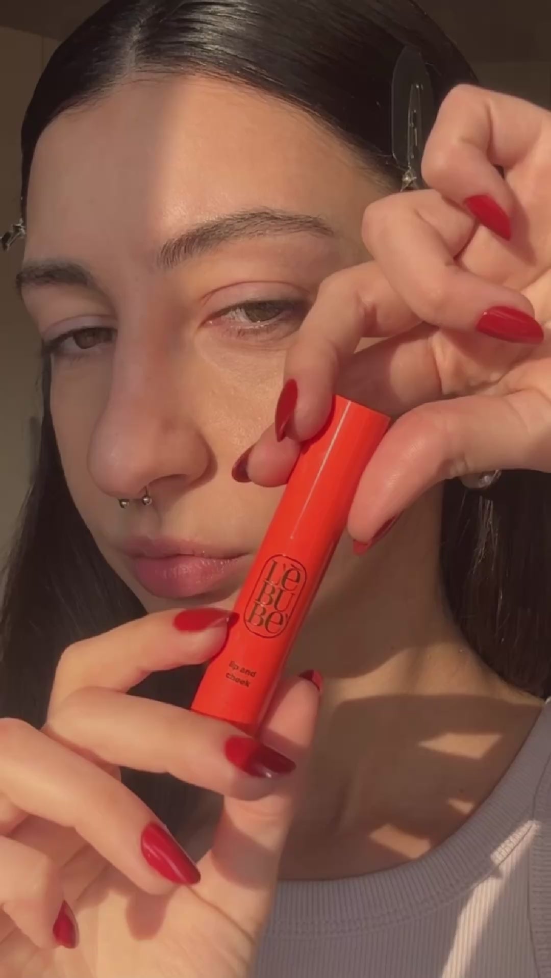 Load video: Woman applying the skincare-infused Lip and Cheek in Fiery Red, a hydrating blush and lipstick that is vegan, natural, Halal