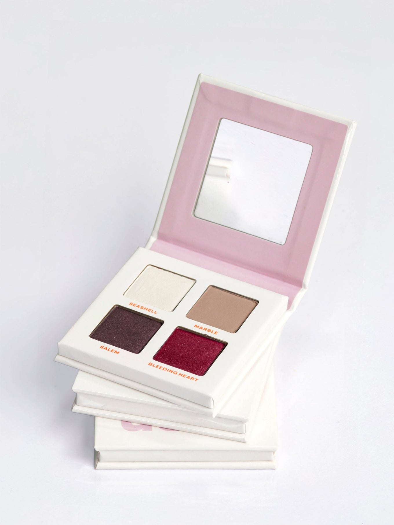 Three stacked DUSK eyeshadow palettes, the top one open showing 4 cool neutral nude eyeshadows in a talc-free vegan formula