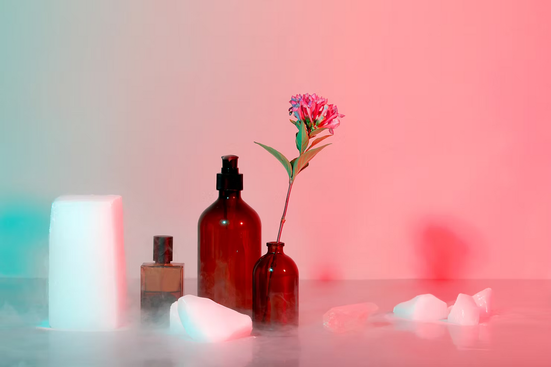 Upcycled beauty products on misty surface: glass bottles, pink flower, ice, pink-blue gradient