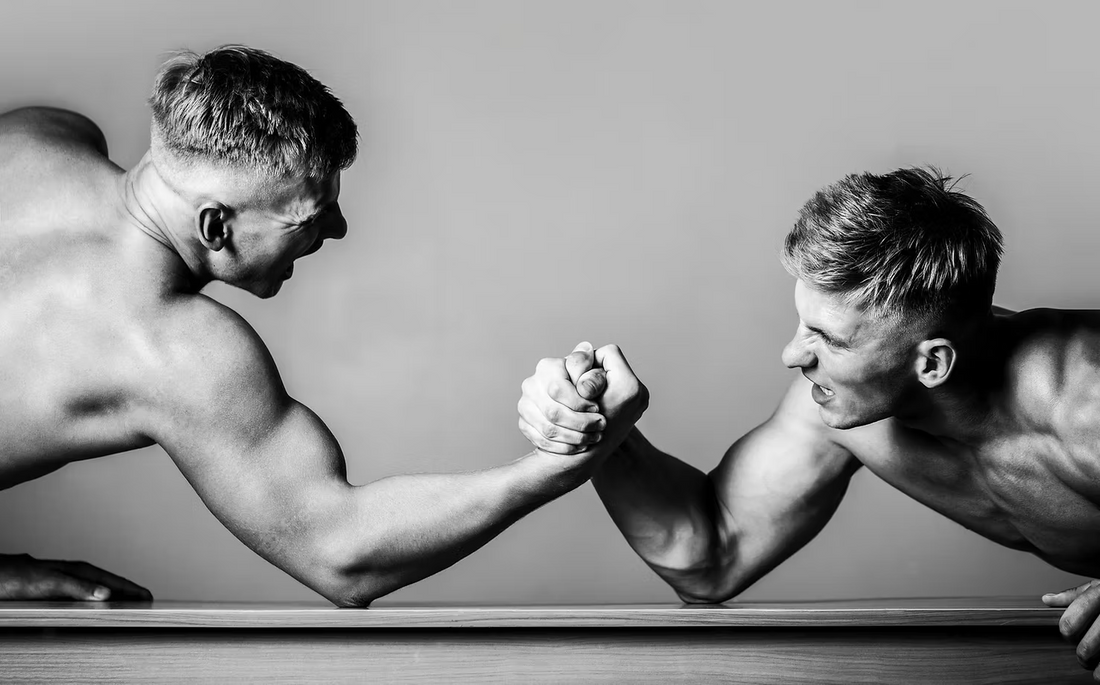 Two muscular men engaged in a fierce arm-wrestling match, symbolizing traditional displays of masculinity and strength.
