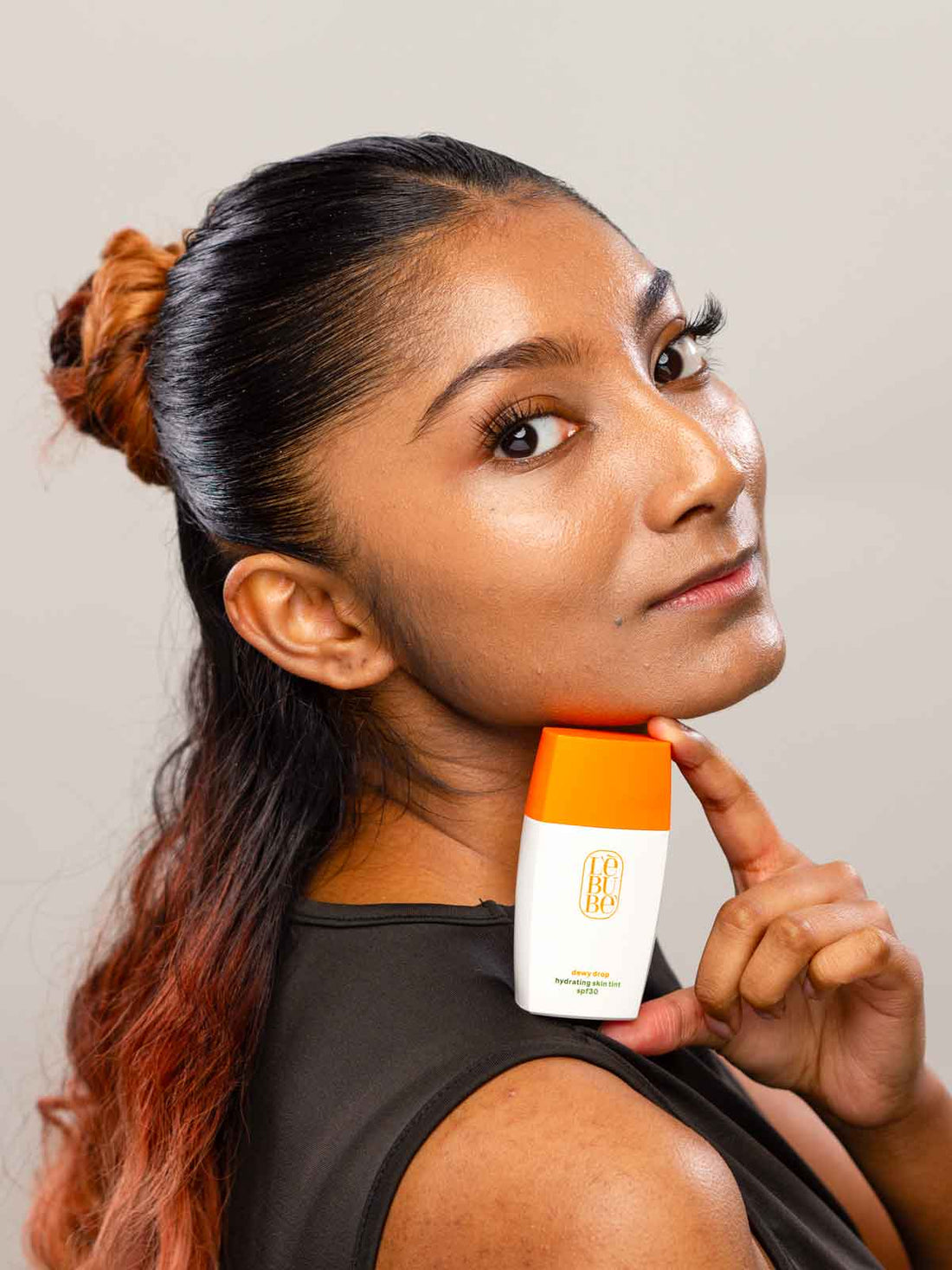 Woman with medium neutral skin wearing and holding Lebubè skin tint with sheer to medium coverage with skincare benefits 