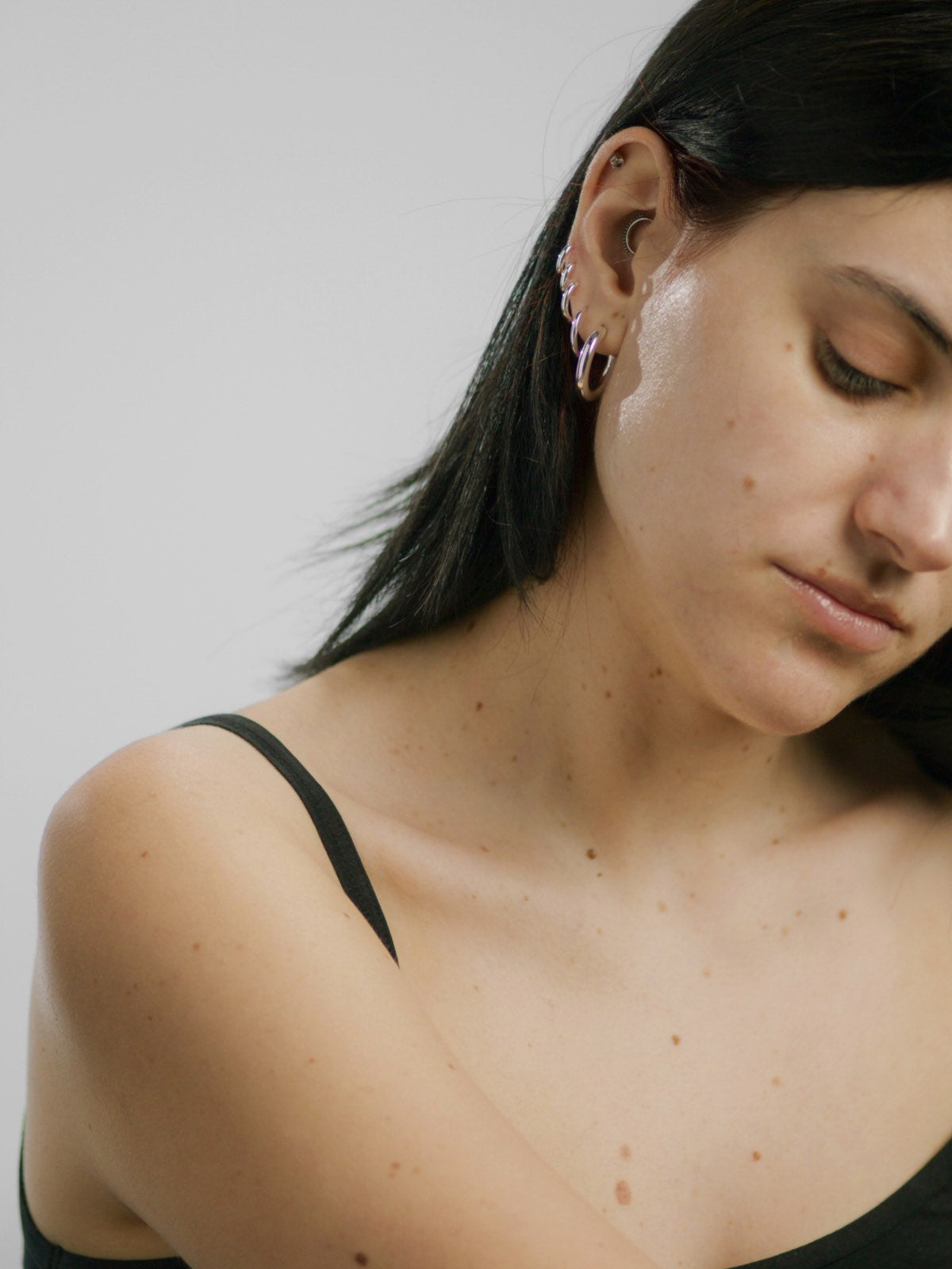 Woman wearing a black strappy top against a plain background before wearing Lebubè vegan hydrating cream highlighter