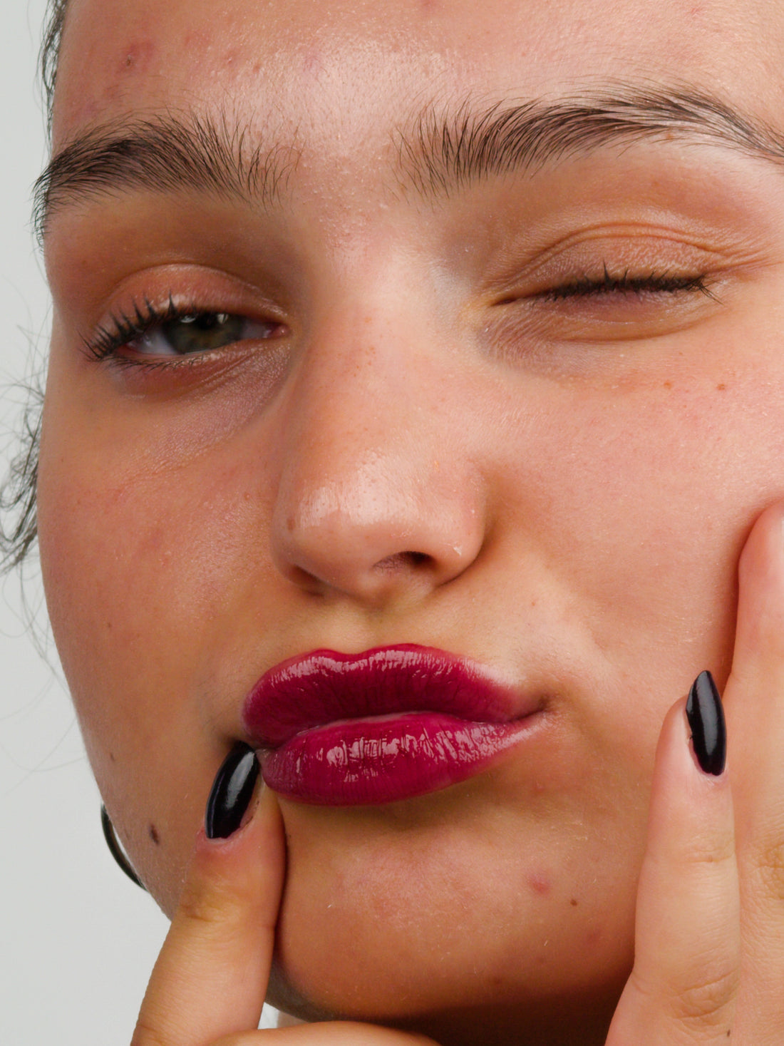 Woman wearing the 2 in 1 vegan lip oil and hydrating lip balm in Erotica shade, with her hands framing her face, by Lebubè.
