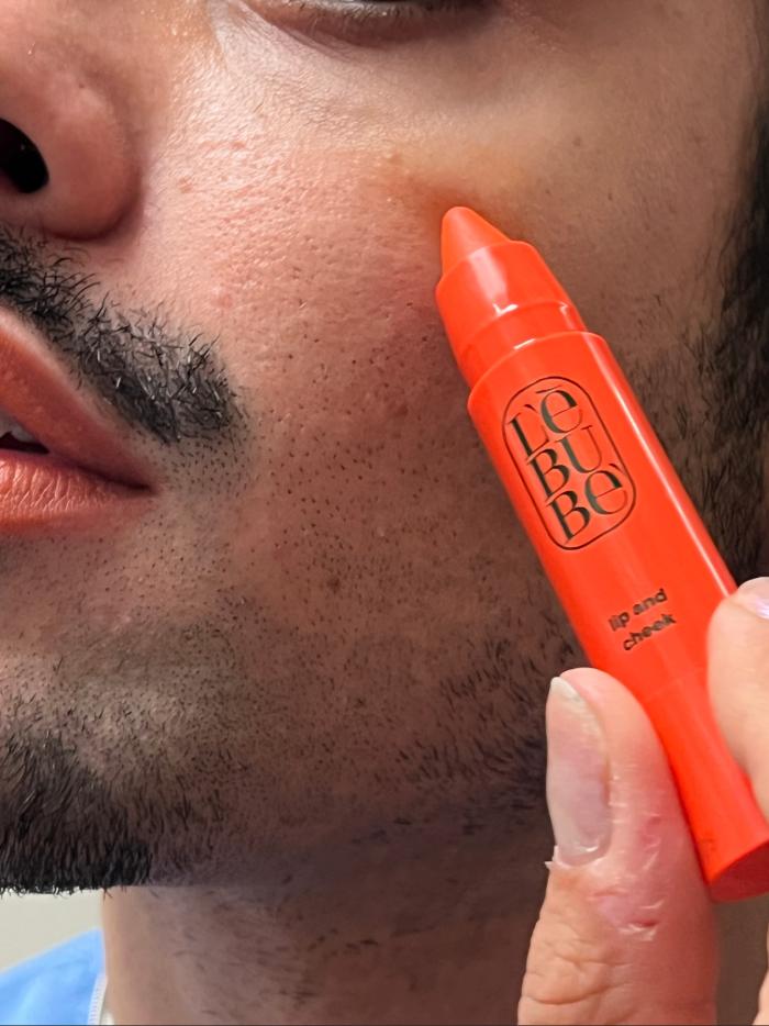 Man applying Lebubè vegan orange blush on his cheeks, for a sunset blush effect and sun-kissed look with skincare benefits