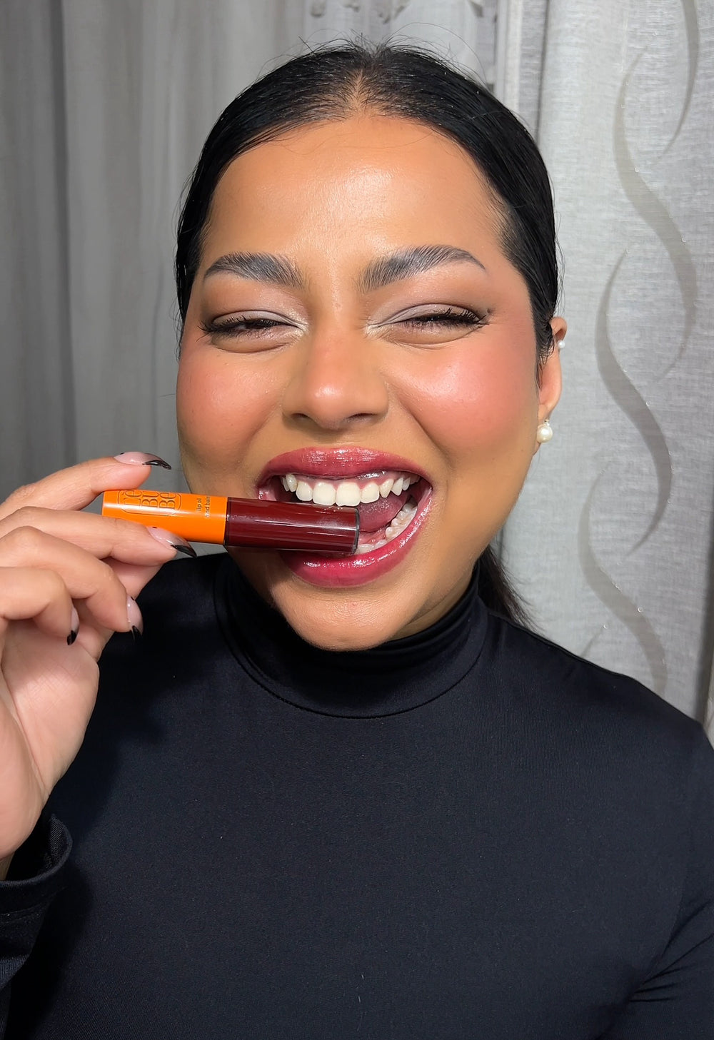 Woman wearing and holding a tinted glossy lip treatment with hyaluronic acid from Lebubè Halal makeup with skincare benefits