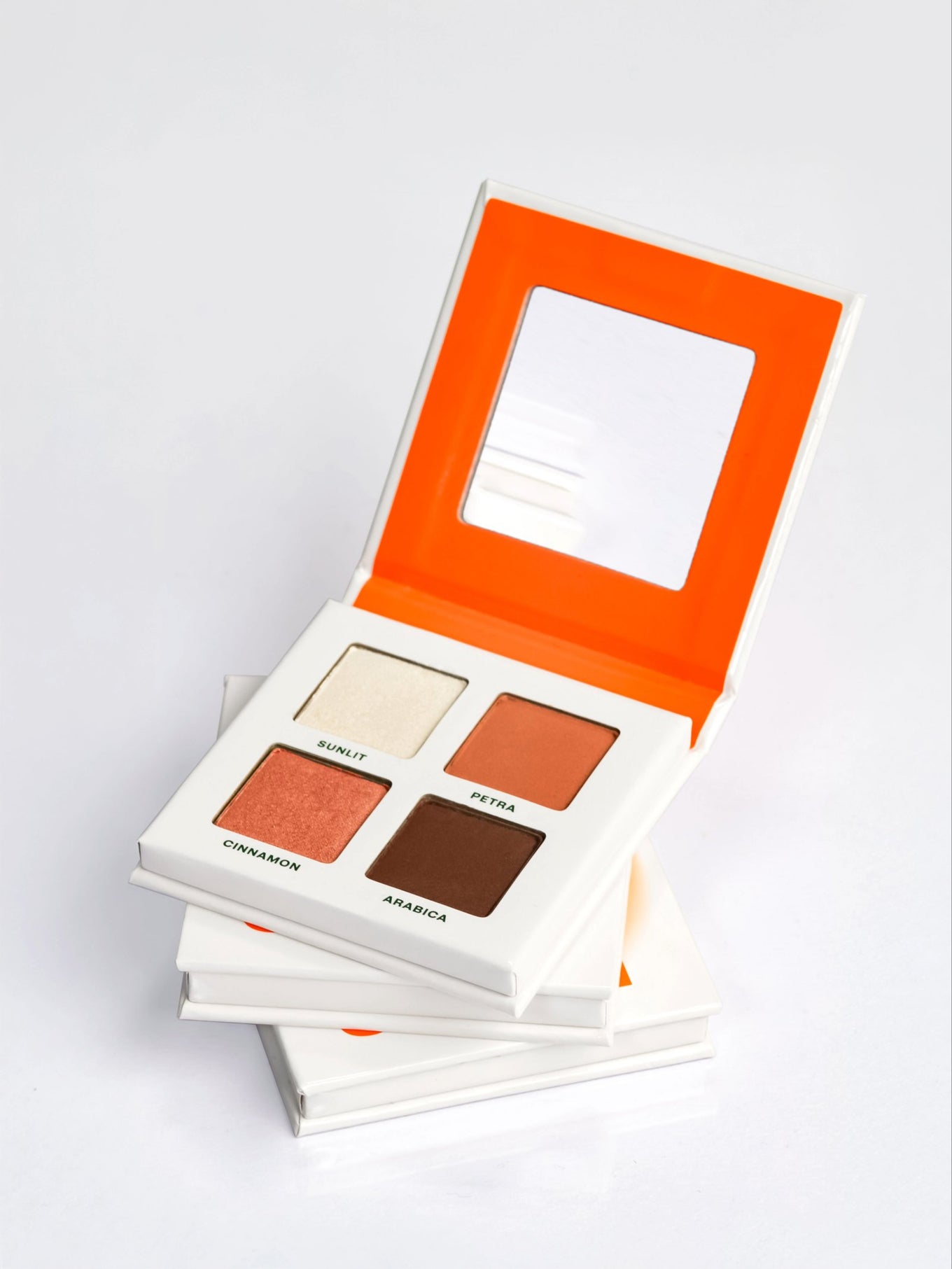 Three stacked DAWN eyeshadow palettes, the top one open showing 4 warm neutral nude eyeshadows in a talc-free vegan formula